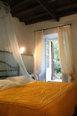 A bedroom with a bed, a window with curtains, a bedside lamp, and a view of greenery outside. - Ospitalità Collicola (Spoleto)