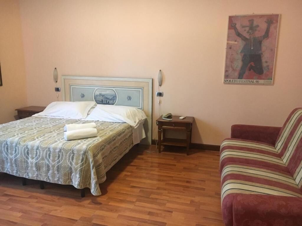 A bedroom with a bed, a nightstand, a red sofa, and a poster on the wall.