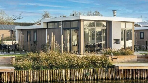 A modern house with a large glass window, a wooden deck, and a water feature in front. - Pavilion Waterfront 8 (Linden)
