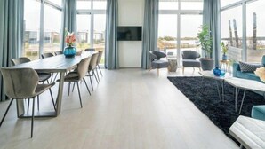 A modern living room with a dining area, large windows, and a flat-screen TV. - Pavilion Waterfront 8 (Linden)