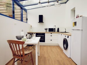 A compact kitchen with a dining area, a washing machine, and a windowed upper section. - Small townhouse in a quiet neighborhood (Coutances)