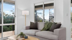 Un salon moderne avec un canapé, une lampe, une table basse agrémentée d’une plante et de grandes fenêtres.