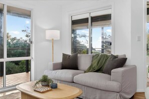 A modern living room with a sofa, a lamp, a coffee table with a plant, and large windows. - The Sellicks Perch Unique Drive On Beach Adventure (Sellicks Beach)