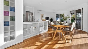 Une cuisine moderne avec des meubles blancs, un coin repas doté d’une table et de chaises en bois, et une grande fenêtre offrant une vue sur la verdure.
