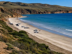 Uma estrada costeira com veículos estacionados na praia, que leva a uma faixa de areia.