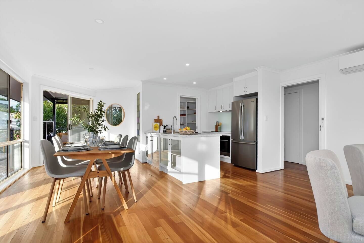 Una cocina moderna con una isla central, una zona de comedor con mesa y sillas de madera, y un ventanal que proporciona luz natural.