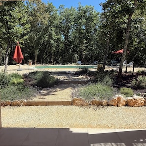 A pool area with a gravel path, surrounded by trees and a red umbrella. - Villa aux Oiseaux, nestled in an oak forest in the Ardèche. Sleeps 8 (Labastide-de-Virac)