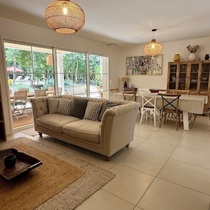 A living room with a sofa, dining table, chairs, and a large window. - Villa aux Oiseaux, nestled in an oak forest in the Ardèche. Sleeps 8 (Labastide-de-Virac)