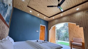 Quarto com cama, teto de madeira, parede azul e vista para o exterior.