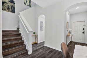Un escalier menant à un palier où se trouve une porte blanche, une petite table avec une plante et un miroir posé sur un support.