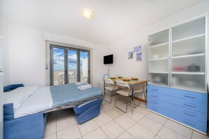 A bedroom with a bed, a desk, chairs, a wardrobe, and a TV. - GuestHost - La Casa al Mare APT 406 with Parking (Lignano Sabbiadoro)