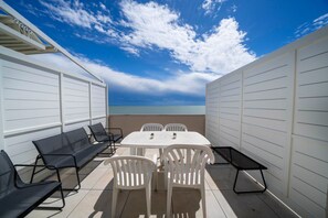 A patio with a table and chairs, a bench, and a view of the sea. - GuestHost - La Casa al Mare APT 406 with Parking (Lignano Sabbiadoro)