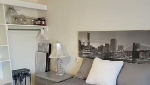 Ett hotellrum med en säng, ett nattduksbord, en lampa, en tavla som föreställer en stadsbild och en vit hylla med dekorativa föremål.