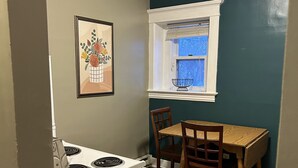 A kitchen with a stove, a dining table with chairs, a window with blinds, and a framed picture on the wall. - Bright apartment in quaint Fargo with refreshing AC (Fargo)
