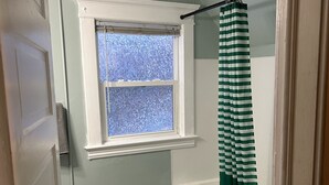 A bathroom with a window, a bathtub, a toilet, and a door. - Bright apartment in quaint Fargo with refreshing AC (Fargo)