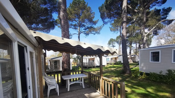 A wooden deck with a table and chairs, surrounded by trees and a grassy area. - 6-person mobile home at a 4-star campground (Lit-et-Mixe)