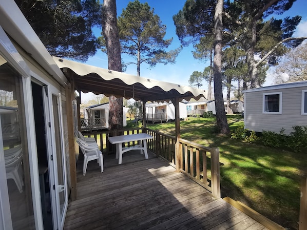 A wooden deck with a table and chairs, surrounded by trees and a grassy area.