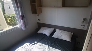 A compact bed with a headboard, a window with curtains, and a small shelf above the bed. - 6-person mobile home at a 4-star campground (Lit-et-Mixe)