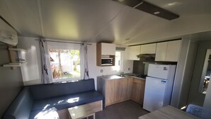 A compact kitchen with a built-in microwave, a sink, and a stove. There's a seating area with a sofa and a small table. - 6-person mobile home at a 4-star campground (Lit-et-Mixe)