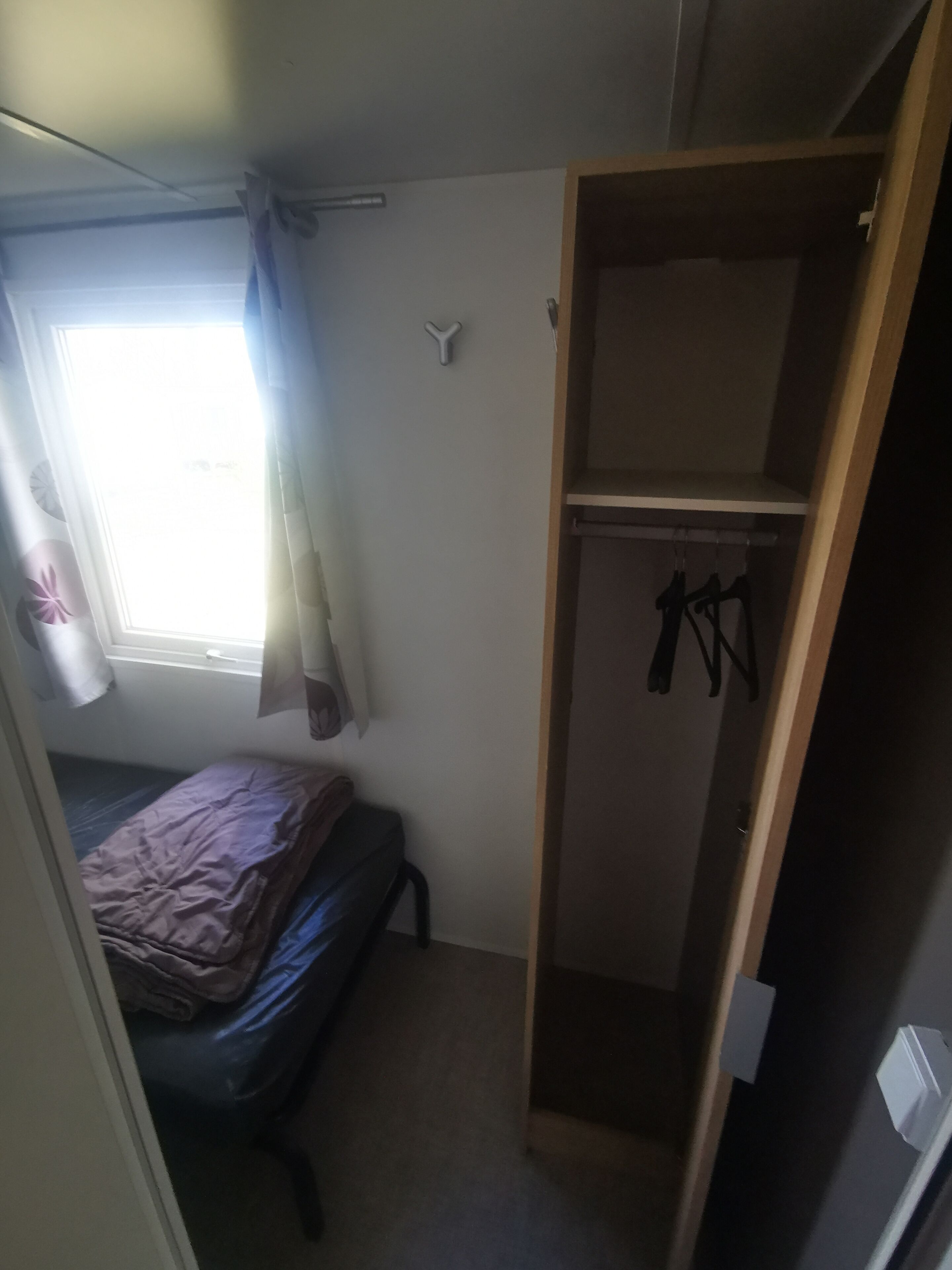 Un dormitorio con cama, armario y ventana con cortinas.