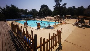 A swimming pool with a wooden deck and a fence, surrounded by trees and shaded areas. - 6-person mobile home at a 4-star campground (Lit-et-Mixe)