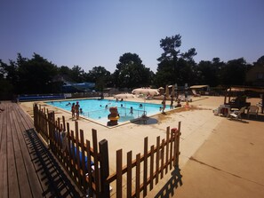 A swimming pool with a wooden deck and a fence, surrounded by trees and shaded areas. - 6-person mobile home at a 4-star campground (Lit-et-Mixe)