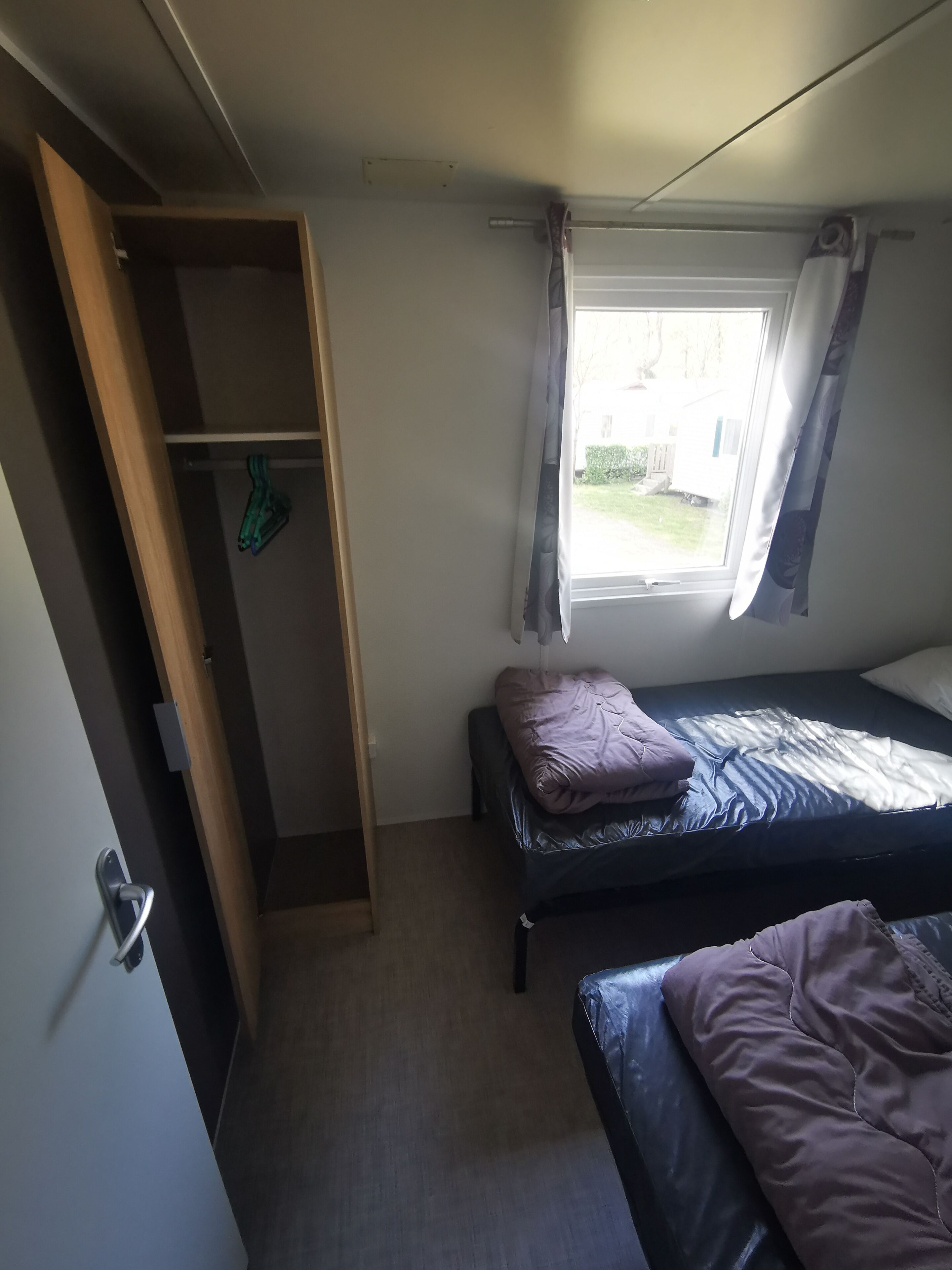 A bedroom with a bed, a wardrobe, a window with curtains, and a view of the outside.