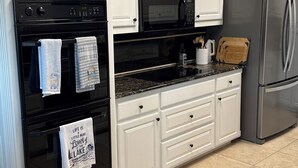 A kitchen with white cabinetry, a black oven, a microwave, a refrigerator, and a granite countertop. - Waterfront Granbury Getaway — 5BR, Dock & Putting Course (Granbury)