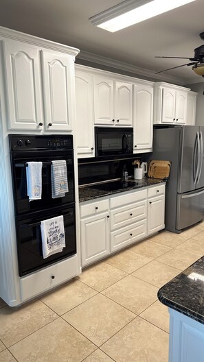 A kitchen with white cabinetry, a black oven, a microwave, a refrigerator, and a granite countertop. - Waterfront Granbury Getaway — 5BR, Dock & Putting Course (Granbury)