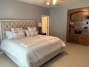 Een slaapkamer met een groot bed, nachtkastje, houten kast en plafondventilator.