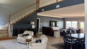 A spacious living room with a staircase, a dining area, and a TV mounted on the wall. - Waterfront Granbury Getaway — 5BR, Dock & Putting Course (Granbury)