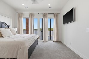 Een slaapkamer met een bed, een aan de muur bevestigde televisie en uitzicht op een balkon met gordijnen.