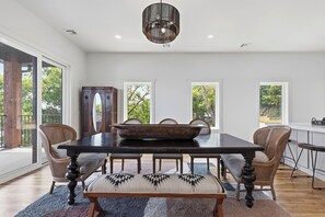 Een eetkamer met een donker houten tafel, geweven stoelen en een grote geweven schaal als decoratie.