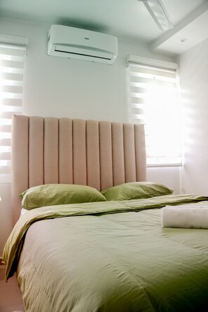 Een slaapkamer met een bed, hoofdbord, airconditioning en een raam met zonwering.