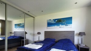 A hotel room with a large bed, a smaller bed, a painting of a landscape, and a mirror. - Comfort 4 Persons (Egmond aan den Hoef)
