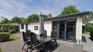 A patio with a table and chairs, a covered umbrella, and a sliding glass door leading to a pool area. - Comfort 4 Persons (Egmond aan den Hoef)