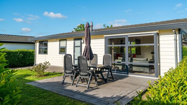 A modern house with a patio, a dining area with chairs and a table, and a glass door leading to a living room. - Comfort 4 Persons (Egmond aan den Hoef)