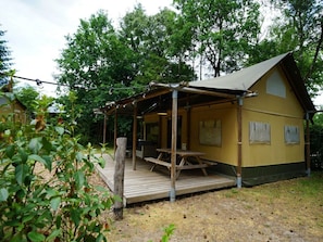 Eine kleine, gelbe Holzhütte mit einer Holzterrasse, einem Picknicktisch und einer überdachten Sitzgelegenheit.