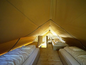 Eine Zelthütte mit zwei Betten, Holzboden und einer zentralen Treppe.