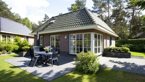 Une maison avec un toit en tuiles, une terrasse avec une table et des chaises, et une pelouse bien entretenue.