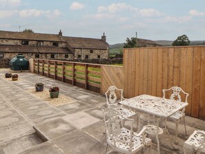 Eine Terrasse mit Steinboden, weißen verzierten Stühlen und Topfpflanzen.