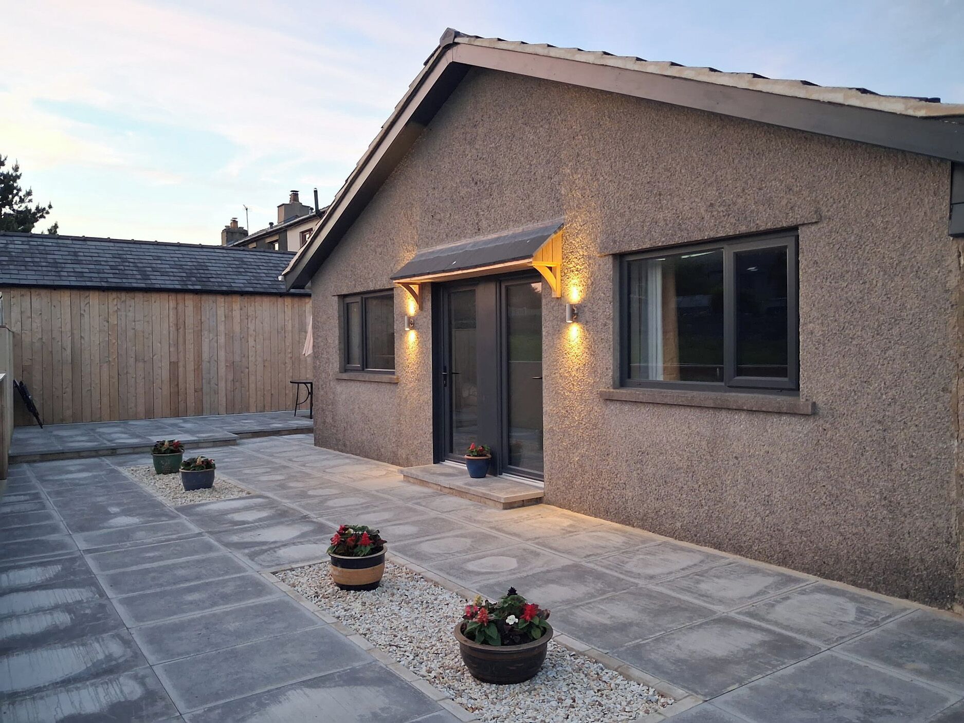 A house with a stone patio, a wooden fence, and potted plants.