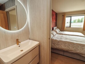 Habitación de hotel con baño, cama con cubrecama estampado, ventana con cortinas y un espejo.