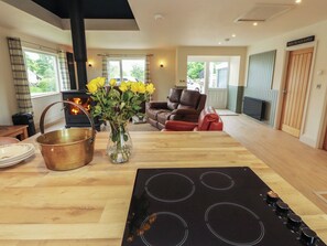 A modern kitchen with a central island, a wood-burning stove, and a dining area with a sofa. - Beckdale (Settle)