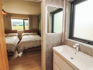 Ein Zimmer mit zwei Betten, einem Badezimmer mit Waschbecken und einem Fenster mit Blick ins Grüne.
