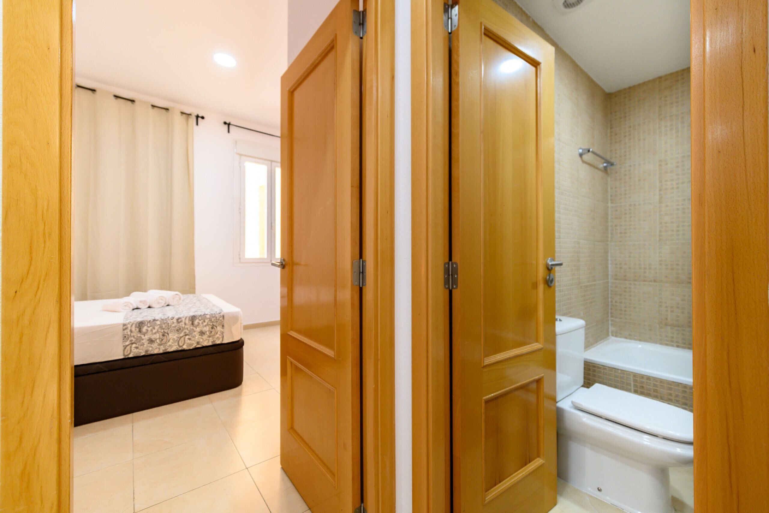 Une chambre avec un lit, une salle de bain avec des toilettes et une baignoire, et des portes en bois.
