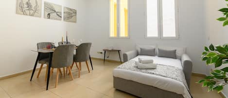A bedroom with a bed, a desk with chairs, and artwork on the wall.