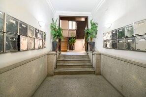 Ein Flur mit Metallschließfächern an beiden Seiten, einer Treppe, die zu einem Raum führt, und Topfpflanzen am Treppenende.