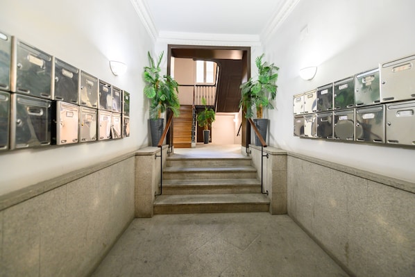 Ein Korridor mit Metallschließfächern an beiden Seiten, einer Treppe und Topfpflanzen.
