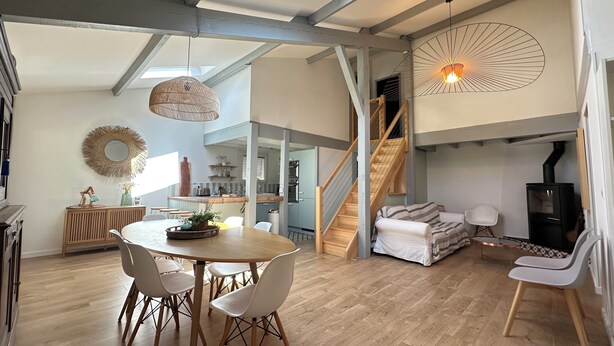 Amplia sala de estar con mesa de comedor, sillas, sofá, escalera y chimenea.
